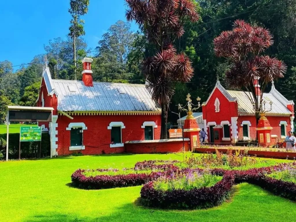 Flower beds in front of a red heritage building in an Ooty garden